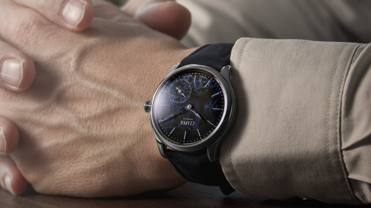 Czapek Promenade Transparencies Aqua Blue worn on the wrist, hands clasped at a table near a window