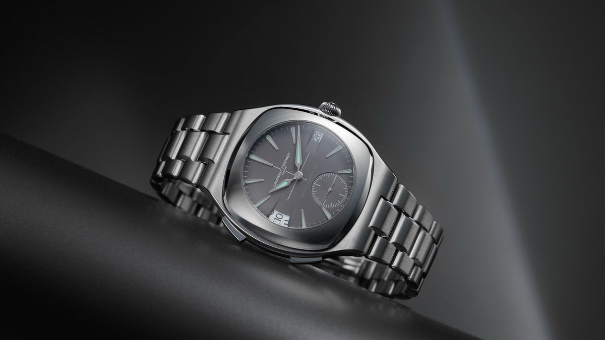 LAURENT FERRIER Sport Traveller Slate Grey resting on a dark curved surface, angled view