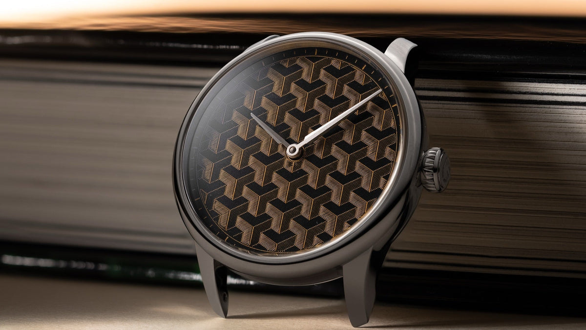 Louis Erard x Wire Art Fil d’Or standing against a book, gold-wire cube dial catching warm light