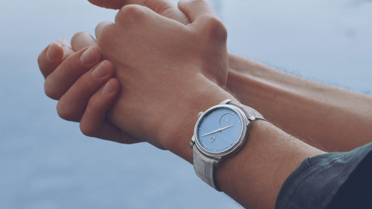 Parmigiani Fleurier TORIC Petite Seconde Platinum Morning Blue worn on the wrist, hands clasped, with water behind