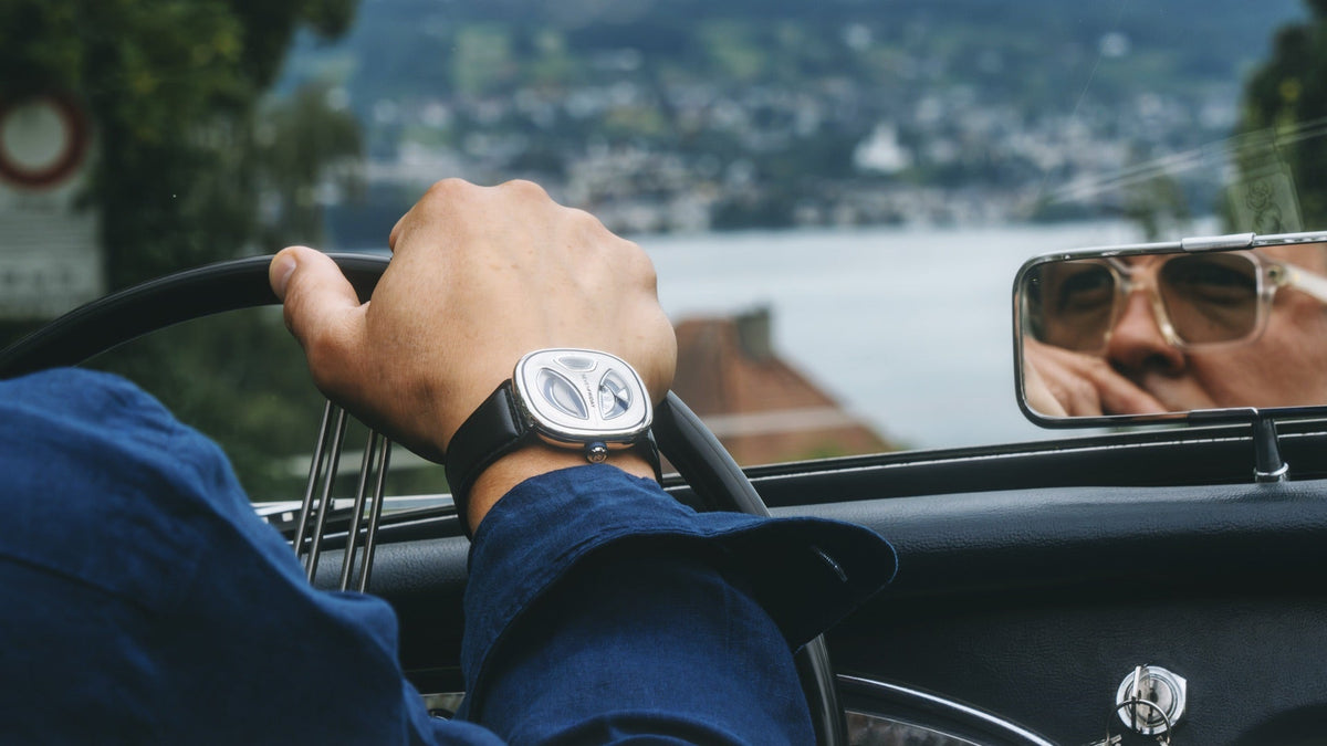 SEVENFRIDAY SF-ME1/01 on the wrist, driving a vintage convertible above a lakeside town