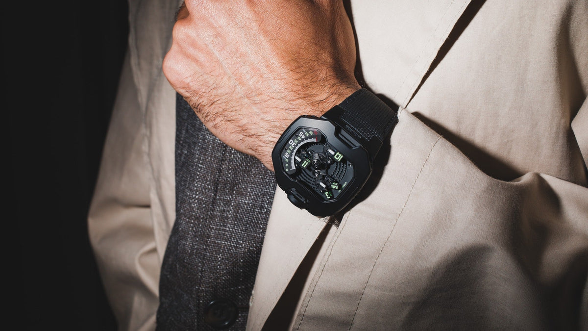 URWERK UR-120 Space Black worn on the wrist under a beige trench coat sleeve